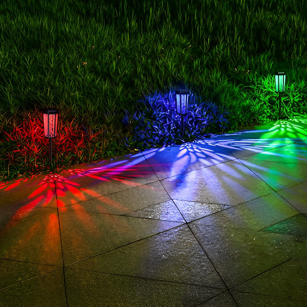 Solar stake light with decorative leaf cutouts, projecting colorful patterns on a lawn at night.
