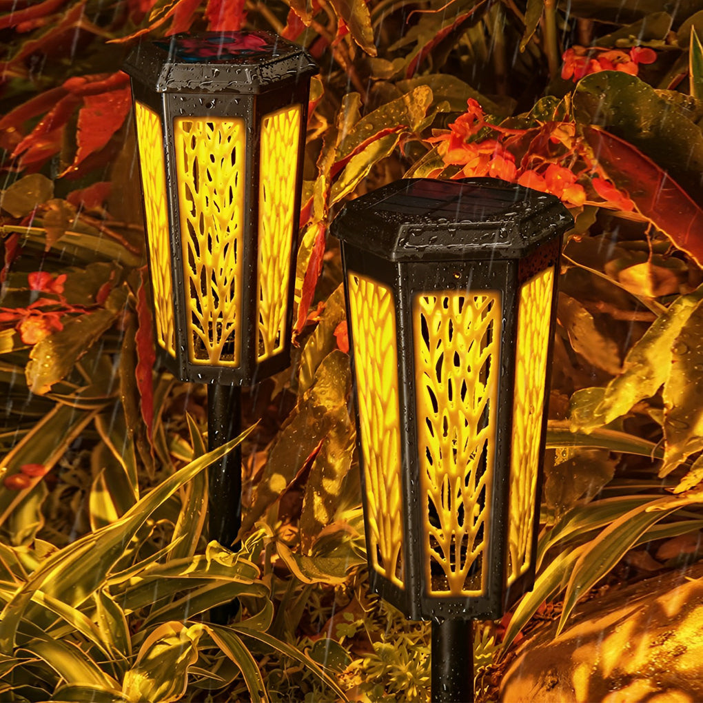 Solar stake light with intricate leaf design, casting colorful patterns on a garden bed at dusk.