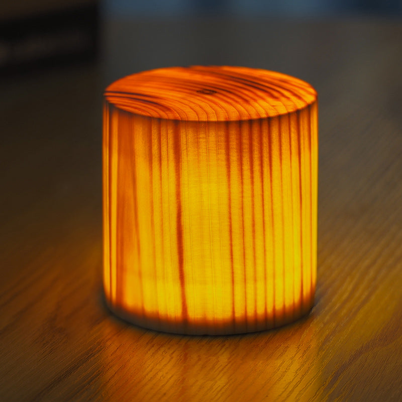Square wood lamp illuminating a collection of wooden lamps on a dark table.
